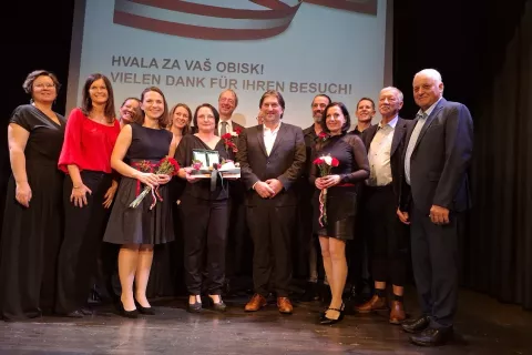 Organizatorji večera, zborovodje in gostje na odru kulturnega doma Slovenskega prosvetnega društva Srce. V sredini predsednica društva Gitti Neuwersch in župan Dobrel vasi Wolfgang Stefitz. / Foto: Jože Košnjek