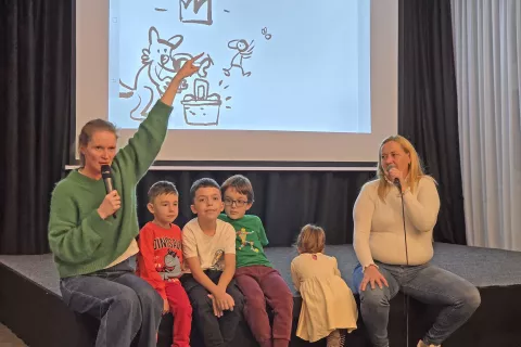 Pripovedovalka Špela Frlic, prevajalka Vesna Berisha in poslušalci, v ozadju so sproti nastajale podobe izpod rok ilustratorja Mihe Hančiča. / Foto: Špela Šimenc