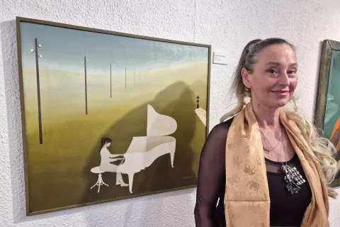 Delo in življenje Alenke Kham Pičman je predstavila hči Norma de Saint Picman. Na sliki je ob materinem olju na platnu z naslovom Krajina s klavirjem (1971). / Foto: Igor Kavčič